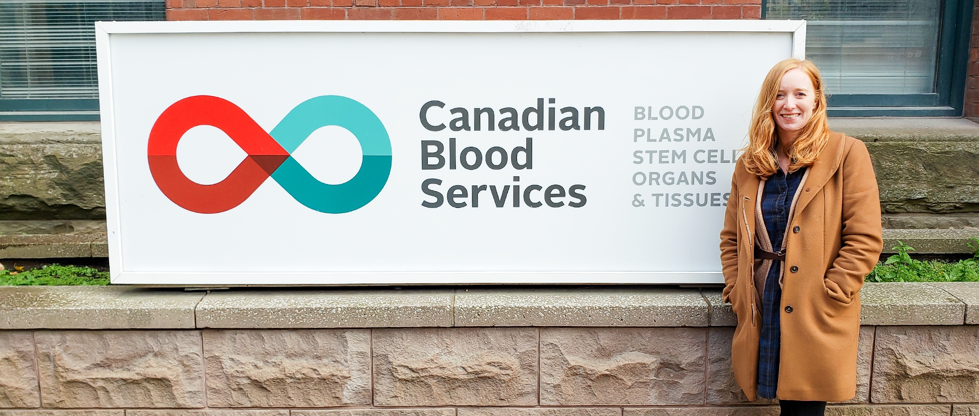 Dr Kelly Holloway standing beside a Canadian Blood Services Sign outside