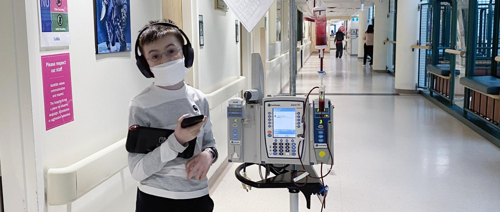 Boy with headphones and mask in hospital hallway getting blood transfusion