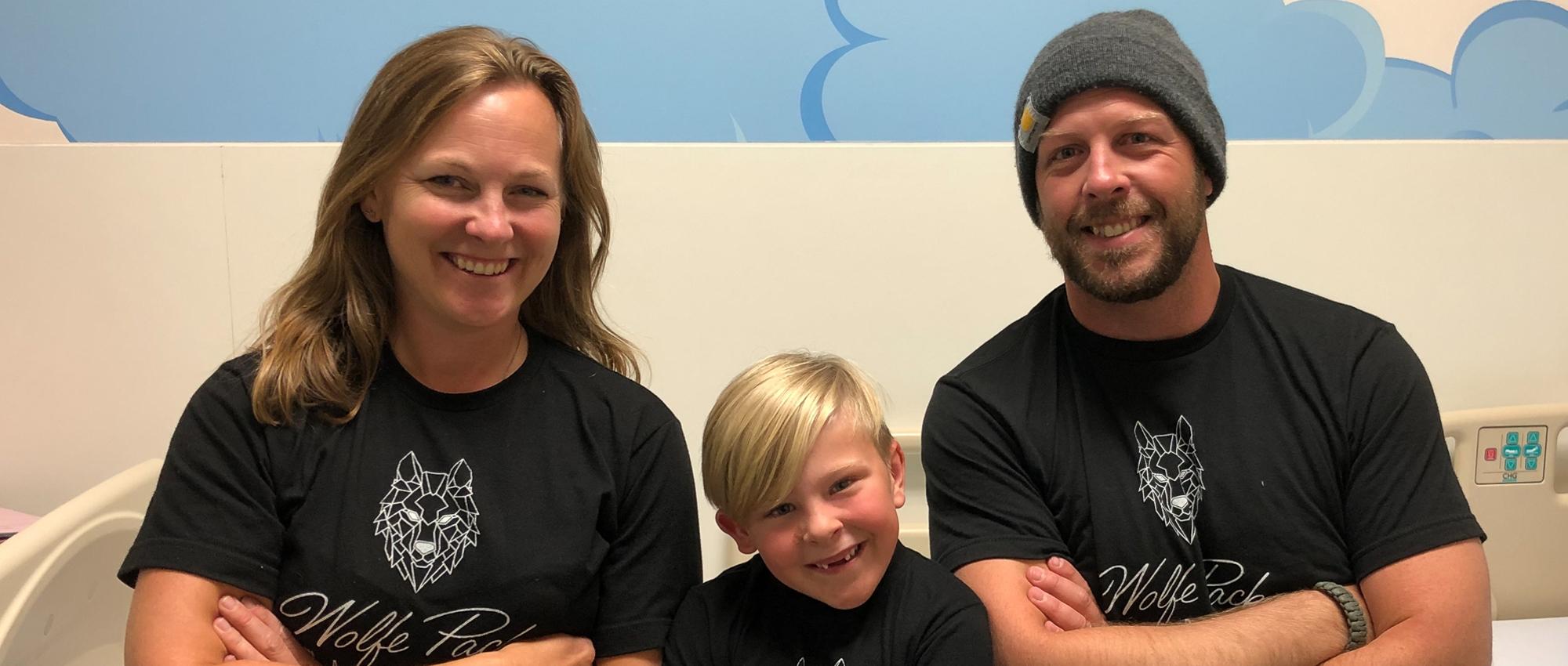 Kristy, Kane and Harrison Wolfe smile in Hospital room wearing Wolfe Pack T shirts