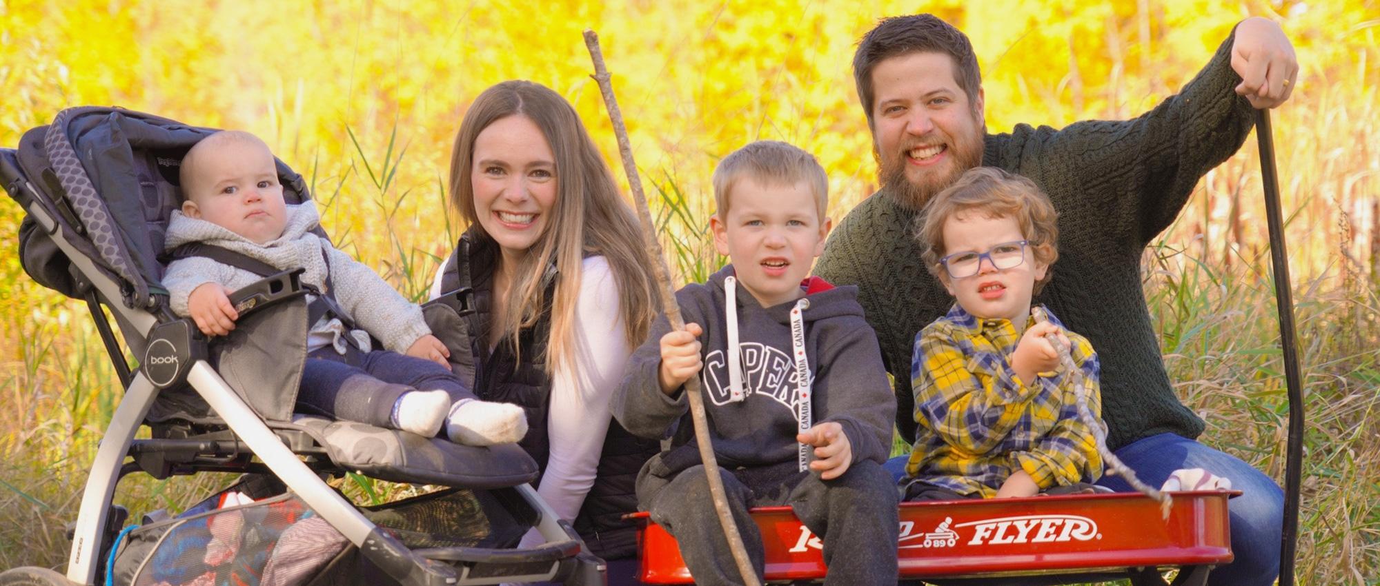 In front of a farm, Lynn Bates and her husband pose with their toddlers in a cart, and their 18-month-old in his trolley.