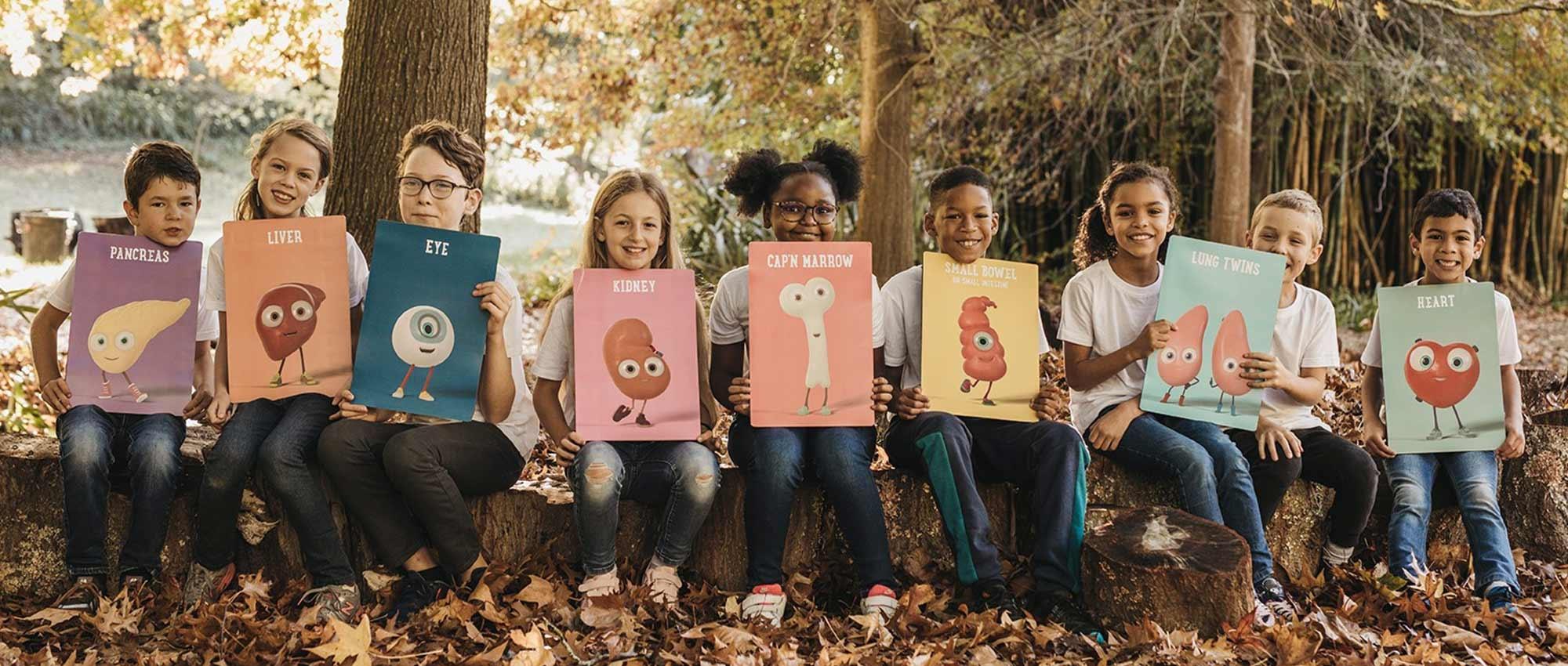 Nine children in a forest each with poster of an Orgamites figure