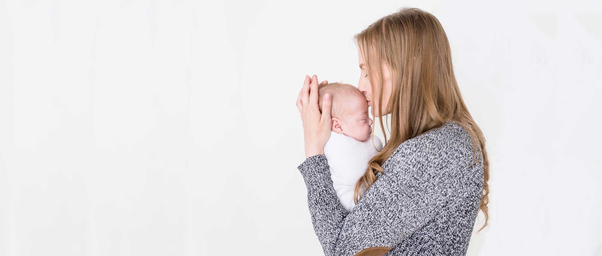 Mother holding swaddled baby and kissing his head