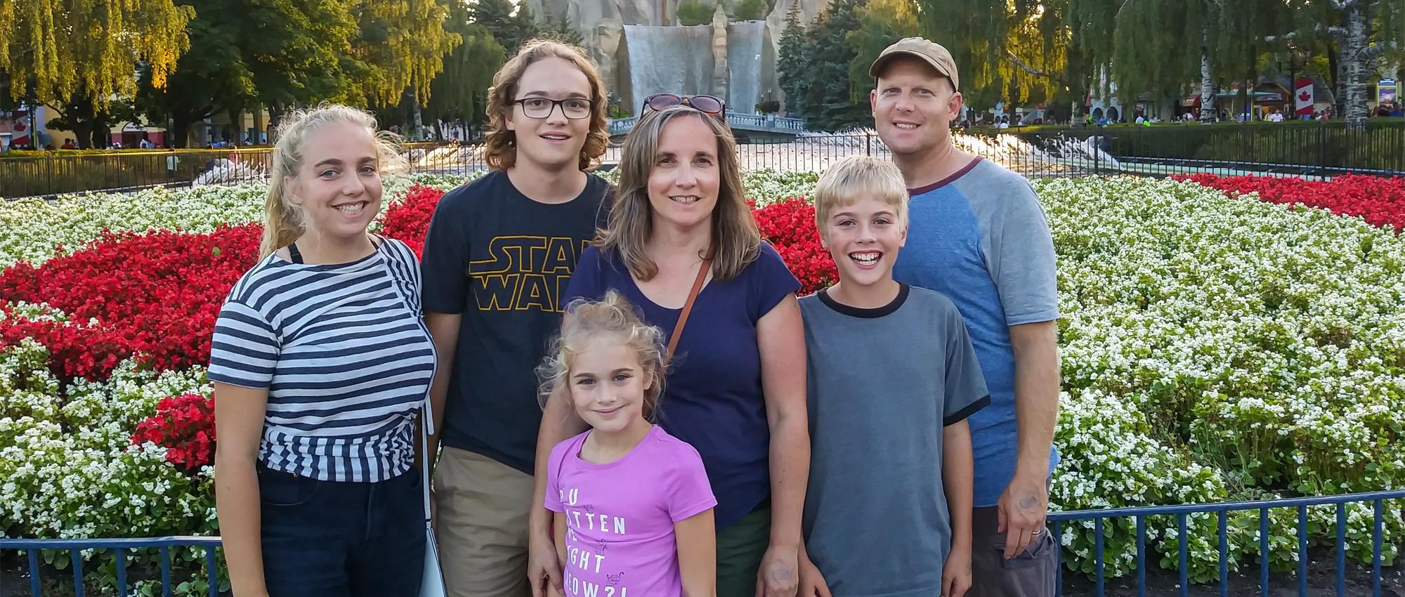 Featured Image of Scott Norton and Nadine Norton with their children and Elsa Norton standing in front of garden of flowers at the amusement park