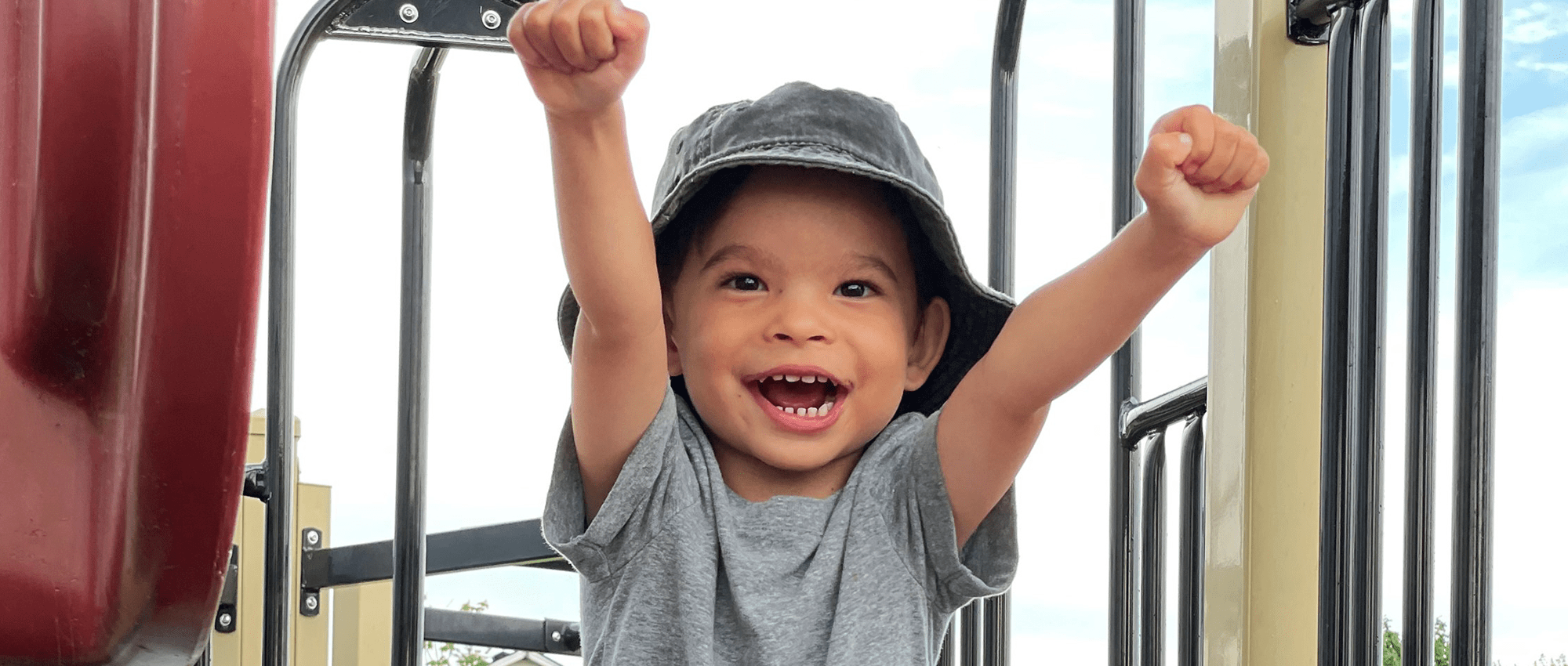Boy smiling with outstretched arms on playground slide. 