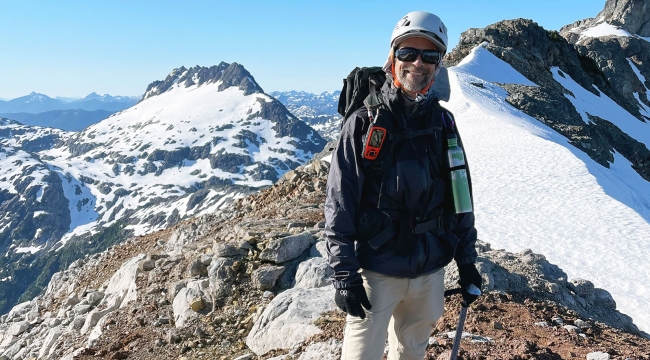 Un homme portant des lunettes de soleil et un casque dans un paysage de sommets montagneux.