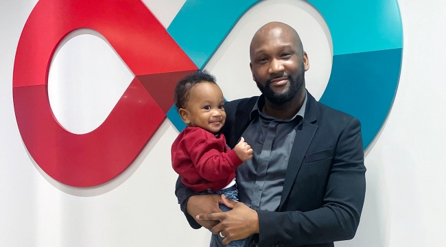 Blood donor holding his one-year-old son in front of Canadian Blood Services logo 