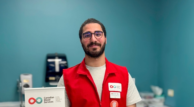 Young man wearing a red volunteer vest standing behind a refreshment counter