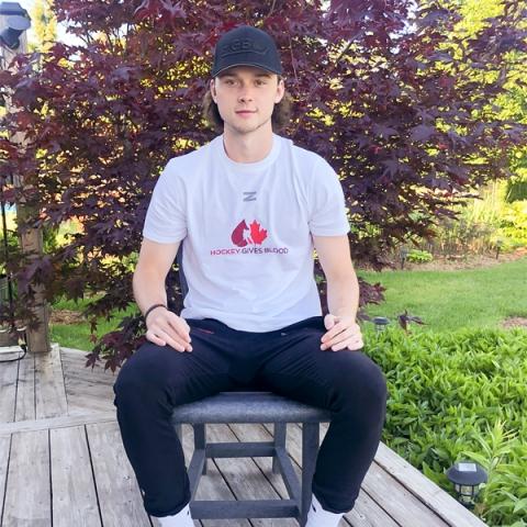 Image of blood donor and registered organ donor Cole Schwindt sitting outside with a white Hockey Gives Blood t-shirt