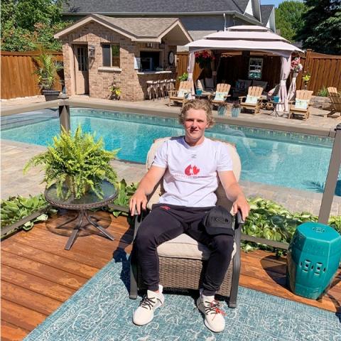Image of blood donor and registered organ donor Ethan Cardwell on a chair by the pool in a white Hockey Gives Blood t-shirt 