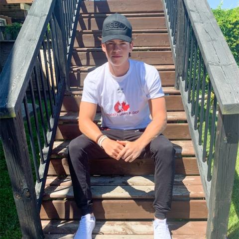 Blood donor Jack Thompson wearing a black cap and a white hockey gives blood t-shirt sitting on the backyard stairs
