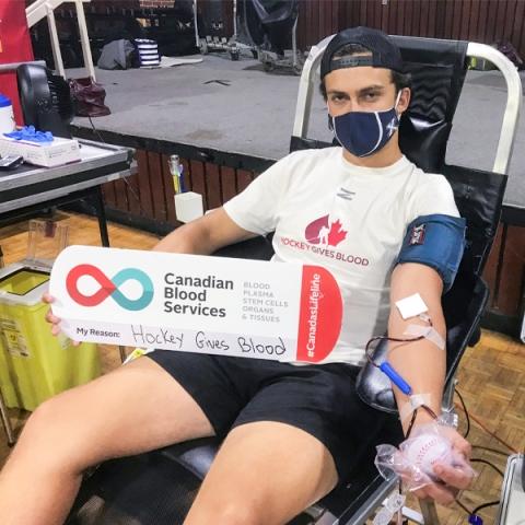 Image of Leif Mattson sitting in a chair donating blood holding a My Reasons sign at the mobile clinics